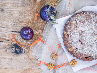 Plum cake with walnuts and fresh ripe plums on white paper over