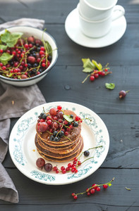 Breakfast set Buckwheat pancakes with fresh berries and honey on rustic plate over black wooden table