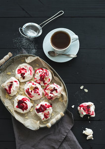 Raspberry and almond meringues with cup of coffee on black rustic wooden table  top view