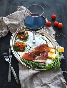 Wine appetizer set Glass of red wine vintage dinnerware brushetta with cherry dried tomatoes arugula parmesan smoked meat on silver tray over rustic grunge surface