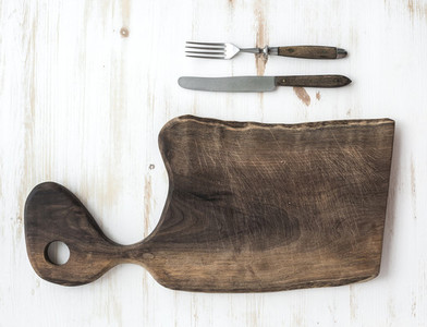 Kitchen ware set  Old rustic chopping board made of walnut wood  knife  fork on a white background