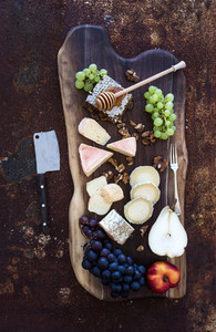 Wine appetizers set French cheese selection  honeycomb  grapes  peach and walnuts on rustic wooden board over dark grunge metal background  Top view