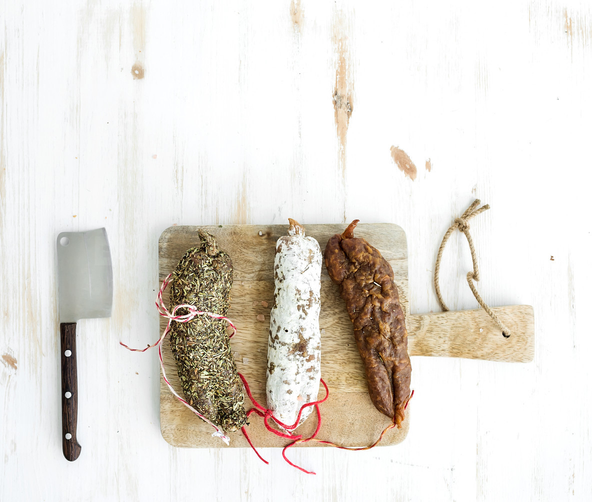 French alsacian smoked salamis on rustic wooden chopping board over white backdrop  top view