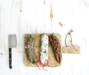 French alsacian smoked salamis on rustic wooden chopping board over white backdrop top view
