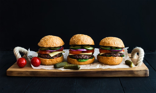 Fresh beef burgers on paper over rustic wooden tray black background