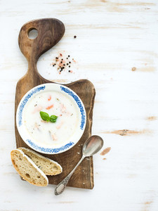 Scandinavian salmon soup with cream  fresh basil and bread in vintage ceramic plate on wooden serving board over white background  top view