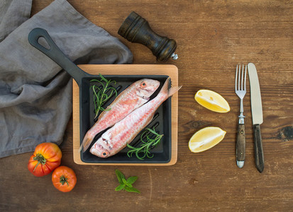 Raw uncooked Red Mullet fish in a cooking pan with rosemary lemon and garlic over rustic wooden background