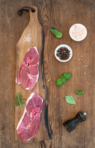 Raw fresh meat lamb entrecote and seasonings on cutting board over rustic wooden background