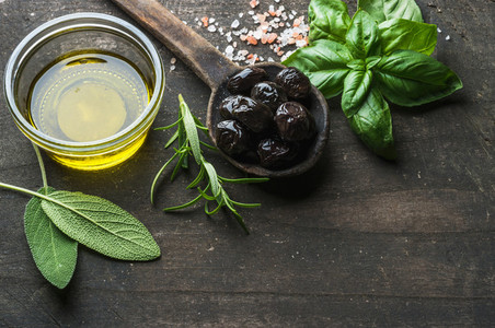 Greek black olives fresh herbs and oil on dark rustic wooden background