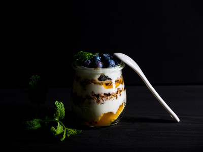 Yogurt oat granola with jam blueberries and mint leavesin glass jar on black backdrop