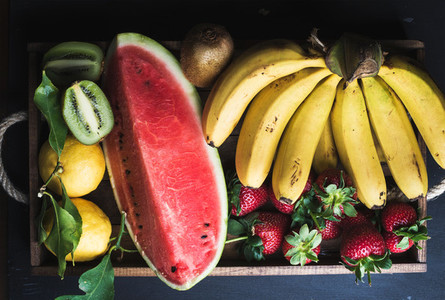 Various colorful tropical fruit selection in wooden tray over dark background