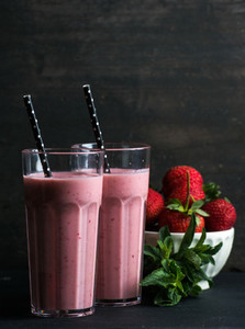 Strawberry and mint smoothie in tall glasses  bawl of fresh berries on dark rustic wood background