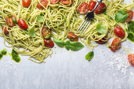 Spaghetti with pesto sauce roasted cherry tomatoes fresh basil and parmesan cheese on steel background