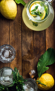 Jug with homemade lemonade mint fresh lemons and ice cubes on wooden background top view copy space