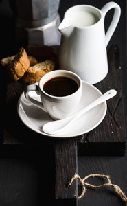 Italian coffee set for breakfast Cup of hot espresso creamer with milk cantucci and moka pot on dark rustic wooden board over black background