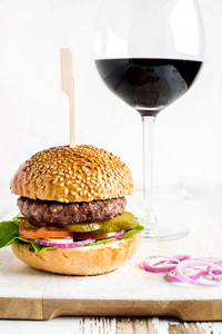 Fresh homemade burger on white wooden serving board with onion rings glass of red wine