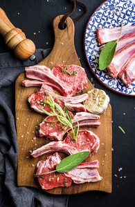 Raw uncooked lamb chops with herbs and spices on rustic wooden board over dark background