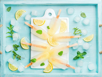 Ice lolly served with lemon slices  fresh mint leaves on white ceramic board over blue Turquoise tray  top view