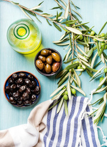 Two bowls with pickled green and black olives olive tree sprigs fresh homemade oil over blue Turquoise background