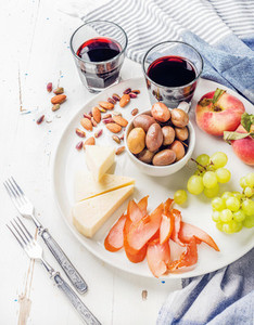 Wine snack set Cheese chicken carpaccio mediterranean olives fruits nuts and two glasses of red on ceramic plate over white wooden background