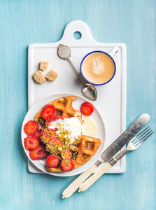 Breakfast set  Warm homemade belgium waffles with whipped cream  strawberry  maple syrup  crushed pistachios  cup of espresso and brown sugar on white ceramic board over blue painted wooden background