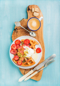 Breakfast set  Warm homemade belgium waffles with whipped cream  strawberry  maple syrup and crushed pistachios  cup of espresso  brown sugar on olive rustic wooden board over blue painted background