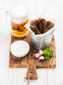 Beer snack set Pint of pilsener in mug open glass bottle rye bread croutons with garlic cream cheese sauce and fresh parsley on rustic wooden board over white painted old background