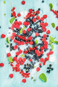 Fresh summer garden berry variety Rasberry black and red currant bilberrry mint on crushed ice over blue background