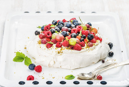 Homemade Pavlova cake with fresh garden and forest berries on white baking tray over light backdrop