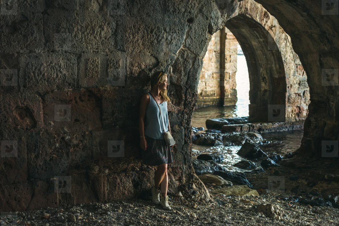 Young blond tourist woman stading in ancient stone shipyard and looking at the sea in the Old city  Alanya  Turkey