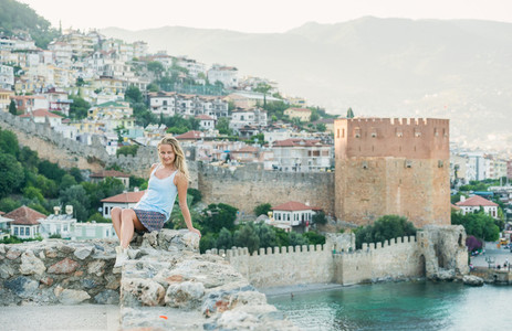 Blond woman sitting on ancient fortress wall Alanya castle Turkey