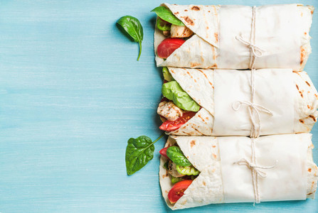 Healthy lunch snack Three tortilla wraps with grilled chicken fillet and fresh vegetables over turquoise blue painted wooden background Top view copy space