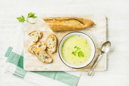 Green vegetable soup with parsley and baguette on white background