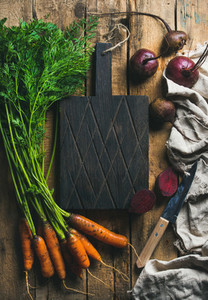 Garden carrots and beetroots with dark cutting board in center