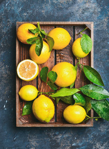 Freshly picked lemons with leaves in rustic wooden tray