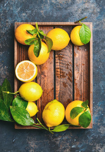 Freshly picked lemons with leaves in wooden tray