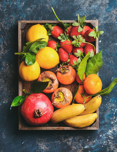 Oranges lemons pomegranate bananas strawberries and persimmon in wooden box