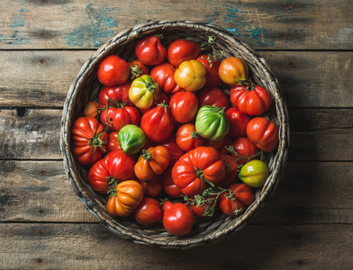 Fresh colorful ripe heirloom tomatoes in basket over wooden background
