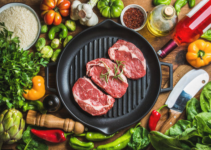 Raw beef steaks in iron pan with vegetables and wine
