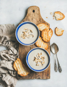 Creamy mushroom soup in bowls with toasted bread marble background
