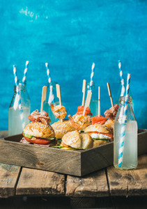 Different homemade burgers with sticks in wooden tray and lemonade