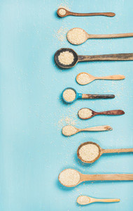 Quinoa seeds in different spoons over blue background copy space