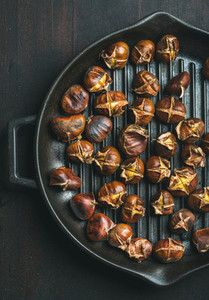 Roasted chestnuts in grilling pan over dark wooden background