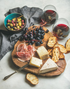 Wine and snack set on wooden board over grey background