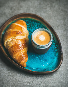 Cup of espresso coffee and croissant in blue ceramic tray