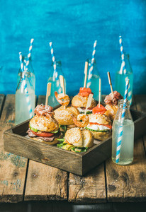 Different burgers with sticks in wooden tray and fresh lemonade