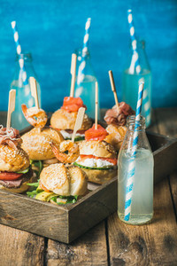 Different homemade burgers with sticks in wooden tray and lemonade