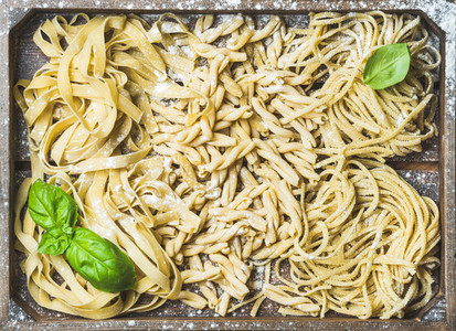 Uncooked Italian pasta in wooden tray with basil and flour