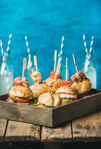 Different homemade burgers in wooden tray and lemonade in bottles