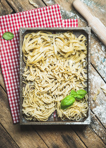 Uncooked Italian pasta in wooden tray over rustic background